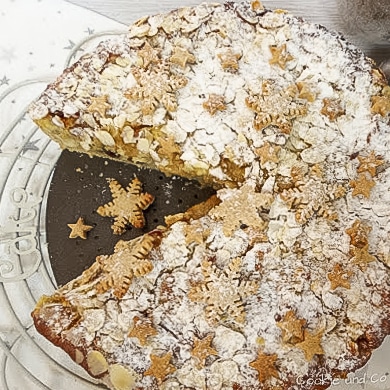 Eine aufgeschnittene weihnachtliche Bratapfel-Tarte auf einem Teller mit Plätzchen im Vordergrund.