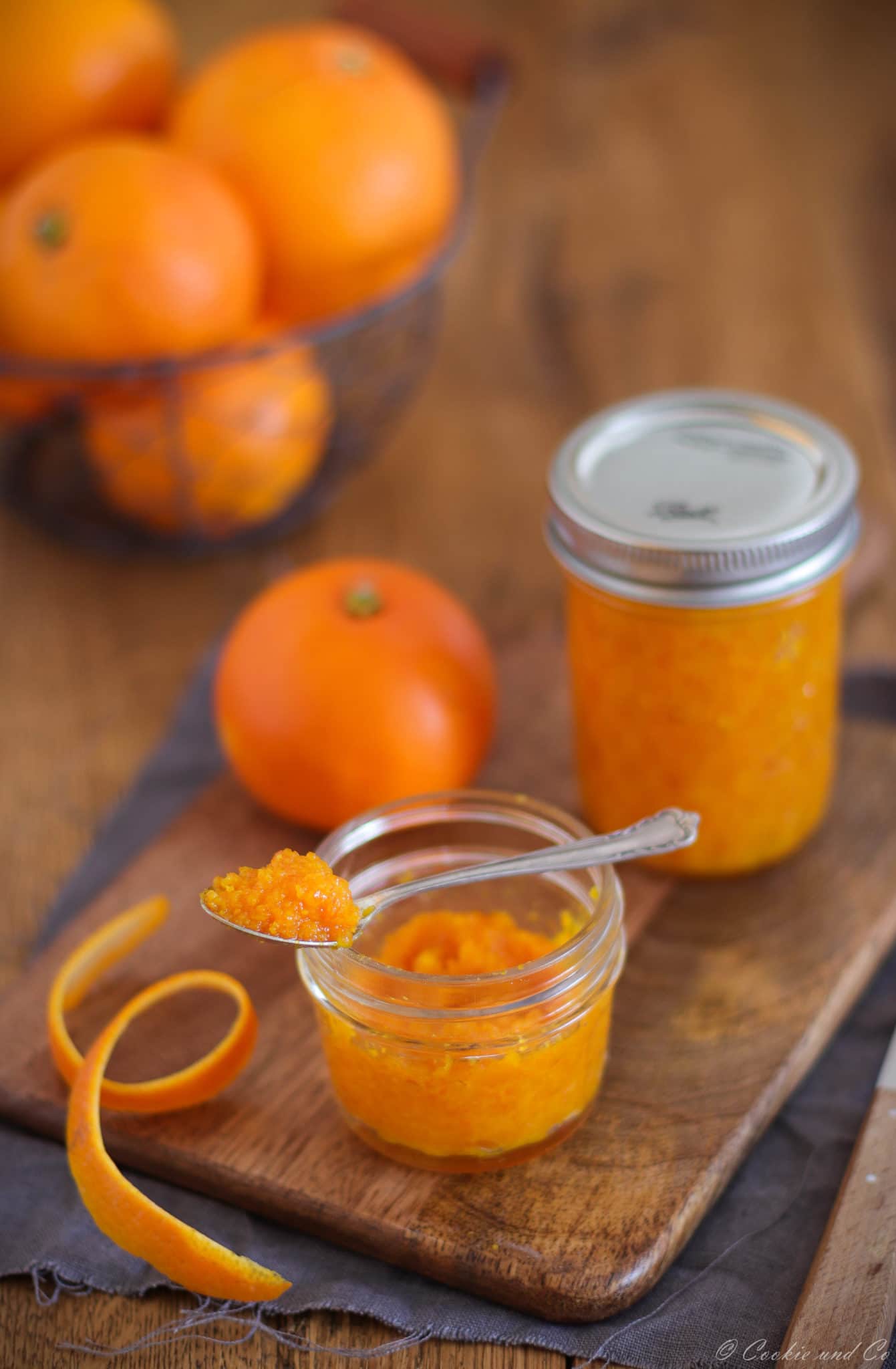 Selbstgemachtes Orangenaroma aus frischen Orangen und Zucker in einem Einmachglas mit Orangen im Hintergrund.