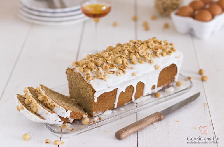 Nusskuchen, dekoriert mit Zucker und Haselnüssen auf einer Kuchenplatte.