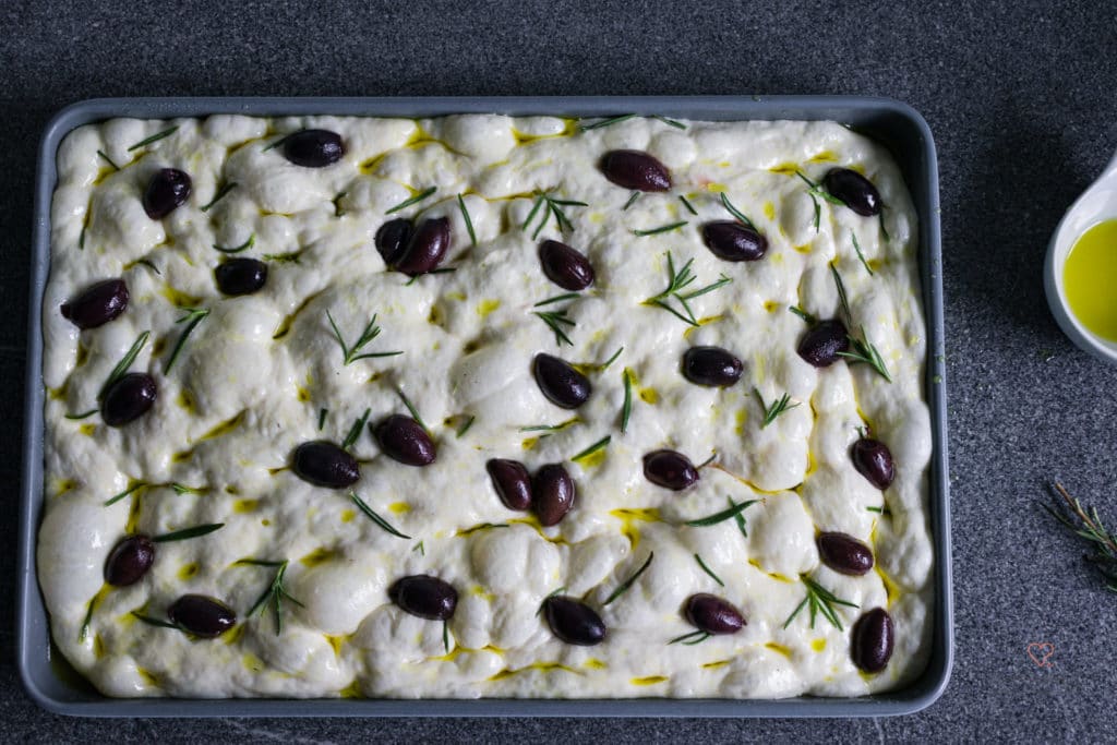 Teig für Focaccia auf einem Blech mit Olivenöl, Rosmarin und Salzflakes