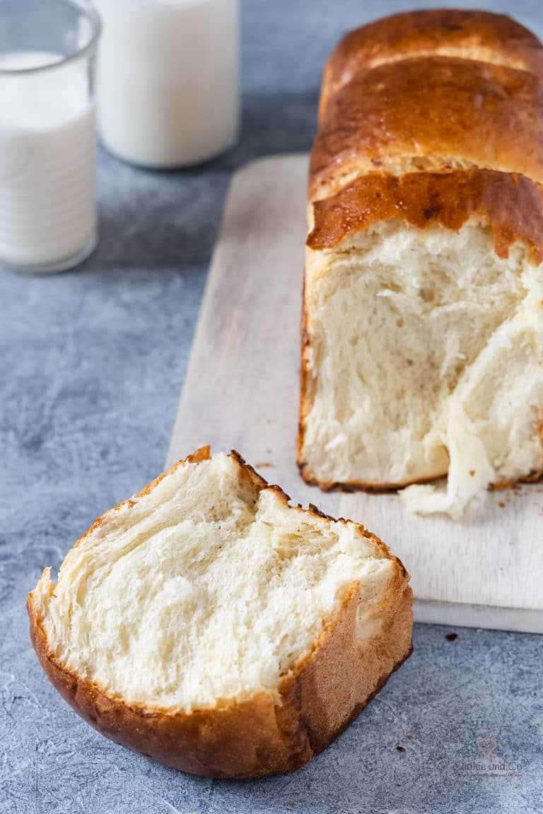 Milchbrot aufgeschnitten auf einem Brett mit einem Glas Milch im Hintergrund.