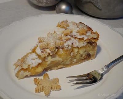 Ein Stück weihnachtliche Bratapfel-Tarte auf einem Teller mit einem Plätzchen und einer Gabel im Vordergrund.