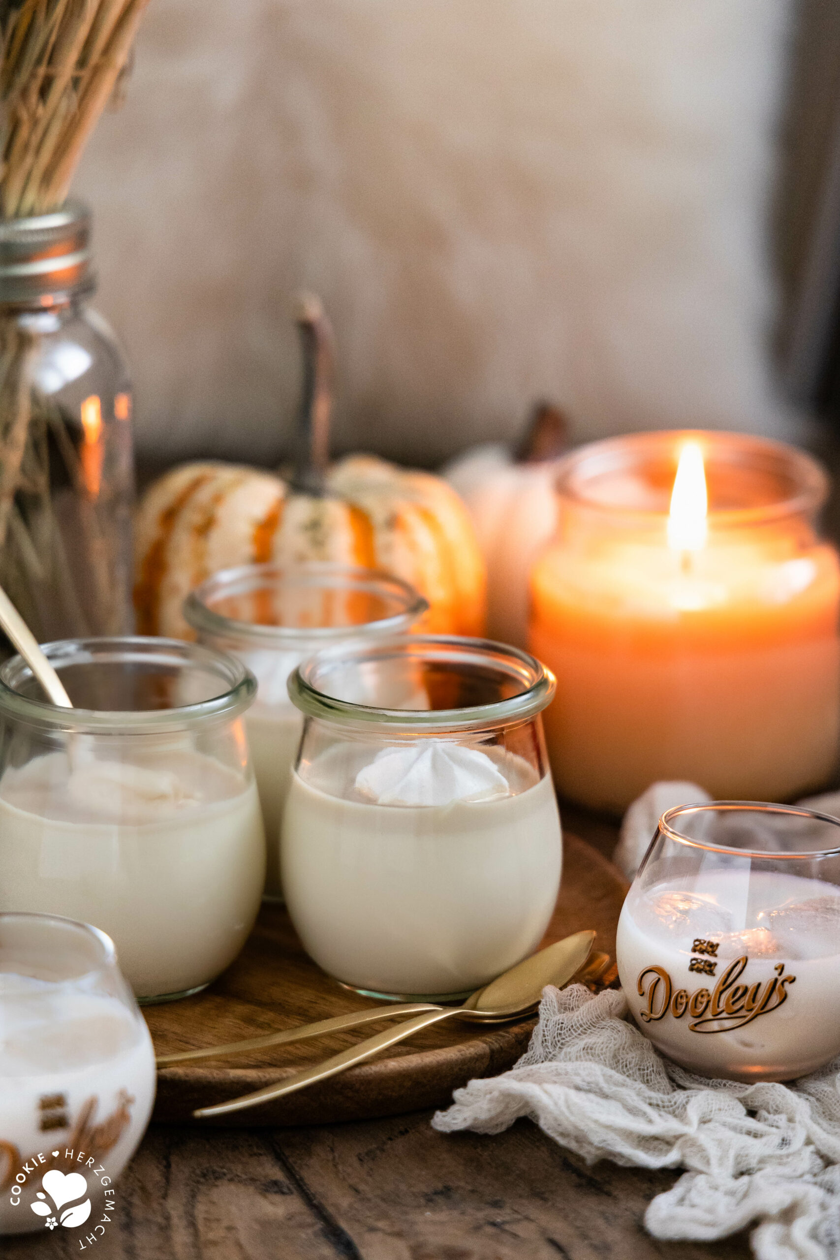 Weiße Schoko-Panna Cotta mit Likör auf einem Holzteller und Kürbissen sowie einer Kerze im Hintergrund.