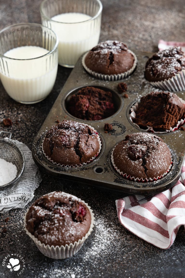 Schoko-Kirsch-Muffins in einer alten Backform mit zwei Gläsern Milch im Hintergrund.