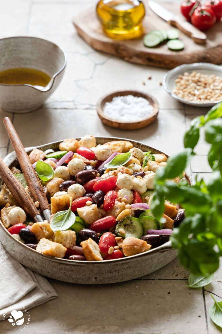 Italienischer Brotsalat „Panzanella“ in einer Salatschüssel, auf den das Dressing mit einem Löffel gegossen wird.