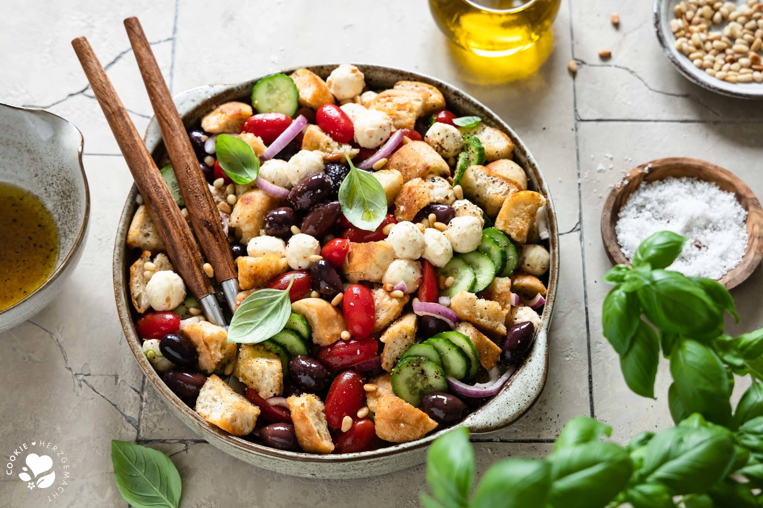 Italienischer Brotsalat „Panzanella“ in einer Salatschüssel mit einem Topf Basilikum im Vordergrund.