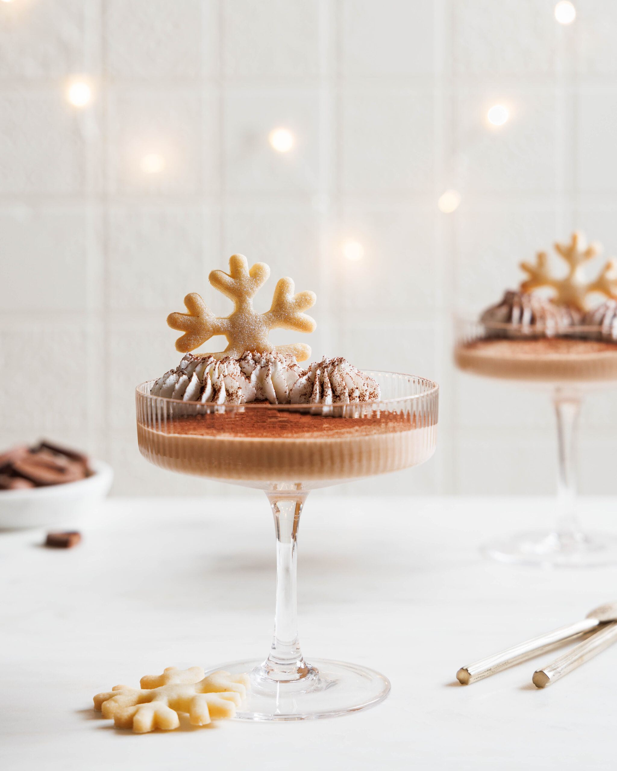 Baileysmousse in einem Champagnerglas, mit Sahne, Kakao und einem Plätzen n Schneeflockenform dekoriert.