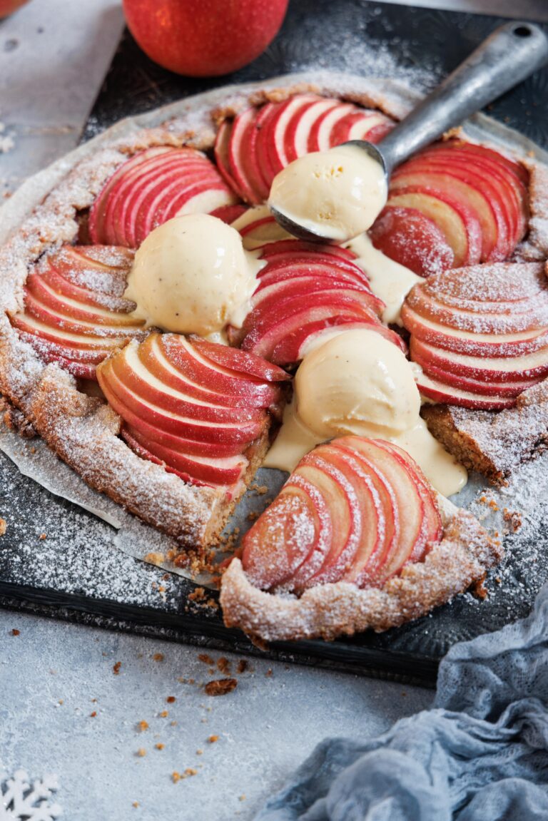 Eine Apfelgalette auf einem Backblech mit leinem Eisportioniere und leicht geschmolzenen Vanilleeiskugeln.