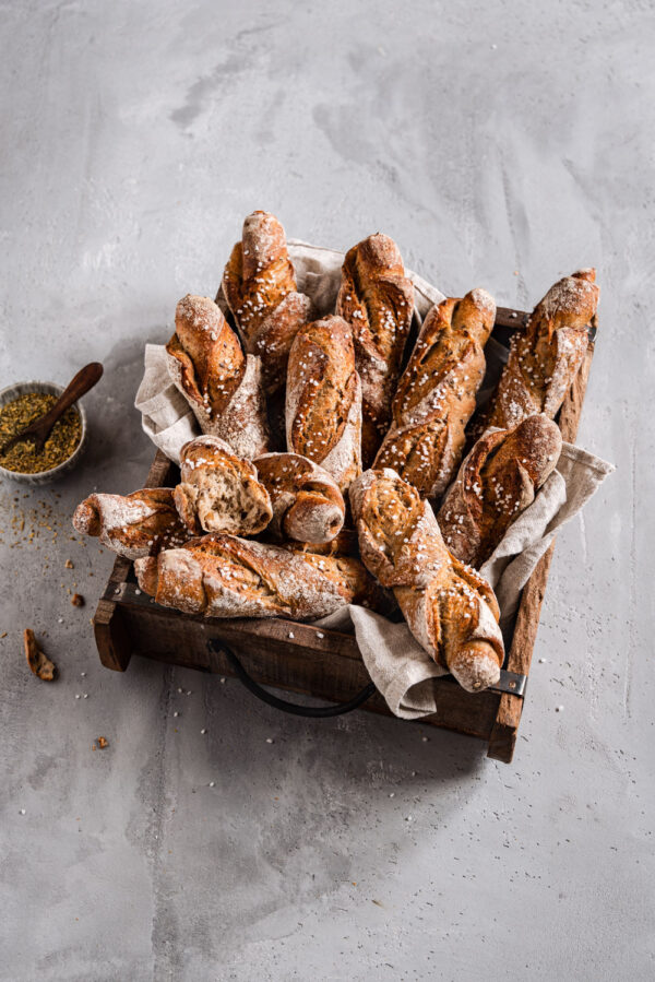 Eine Holzkiste mit Kornstangen-Brötchen und einer Schale mit Brotgewürz daneben.