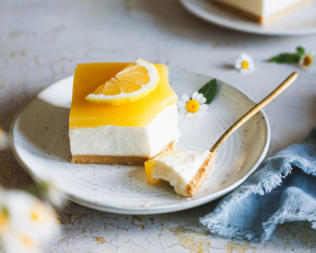 Lemon Cheesecake mit einer Kuchengabel auf einem Teller und weiteren Tellern mit Kuchen im Hintergrund.