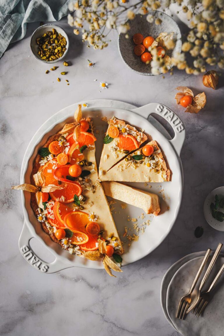 Orangentarte mit Mürbeteigboden und cremiger Füllung und einer Deko mit Orangen, Pistazien, weißer Schokolade und Physalis.