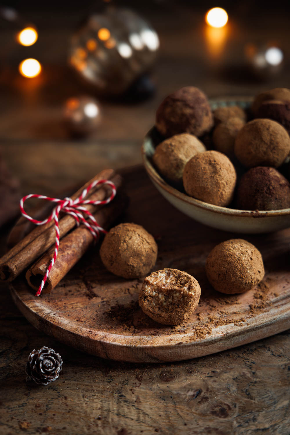 Spekulatiuskonfekt auf rustikalem Holzbrett angerichtet, dekoriert mit Zimtstangen und weihnachtlicher Beleuchtung im Hintergrund – perfekt für die Festtage.